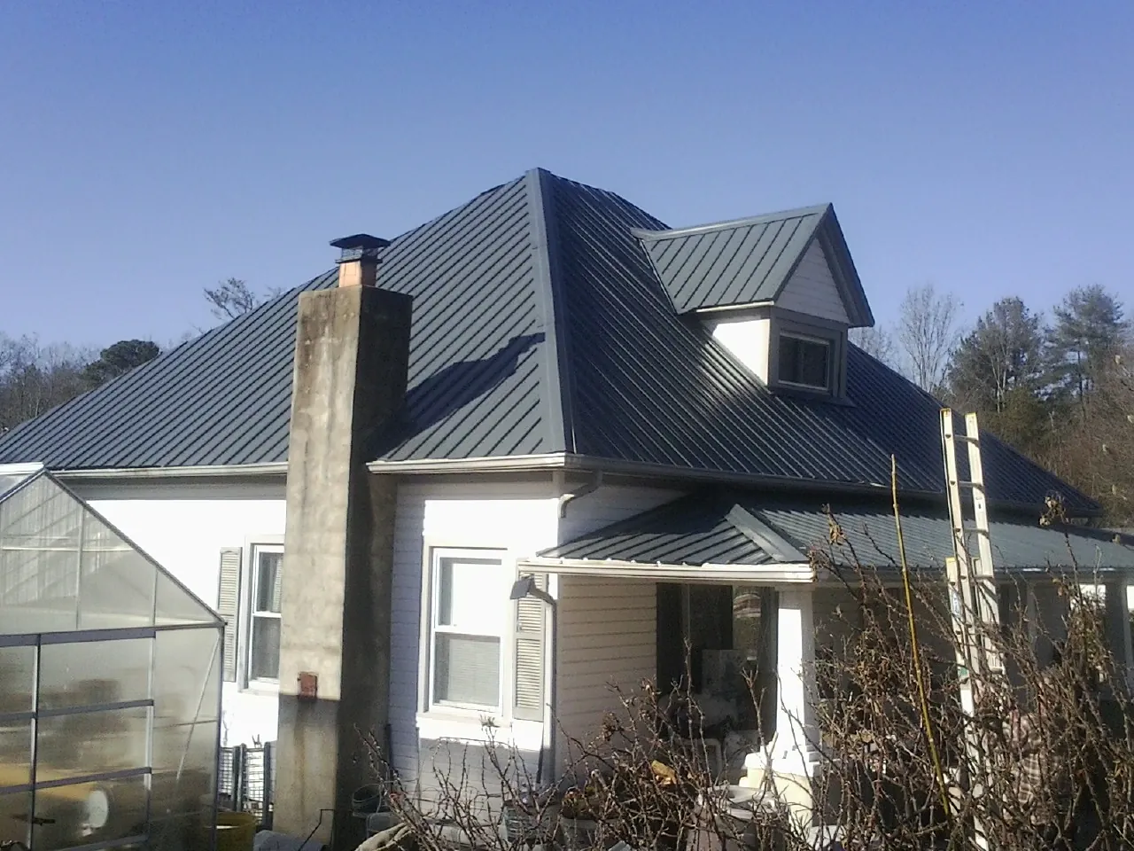Dark blue standing seam metal roof on a white farmhouse with dormer — Slate & Tile Roof Repair by Roofing Brothers in Lucedale
