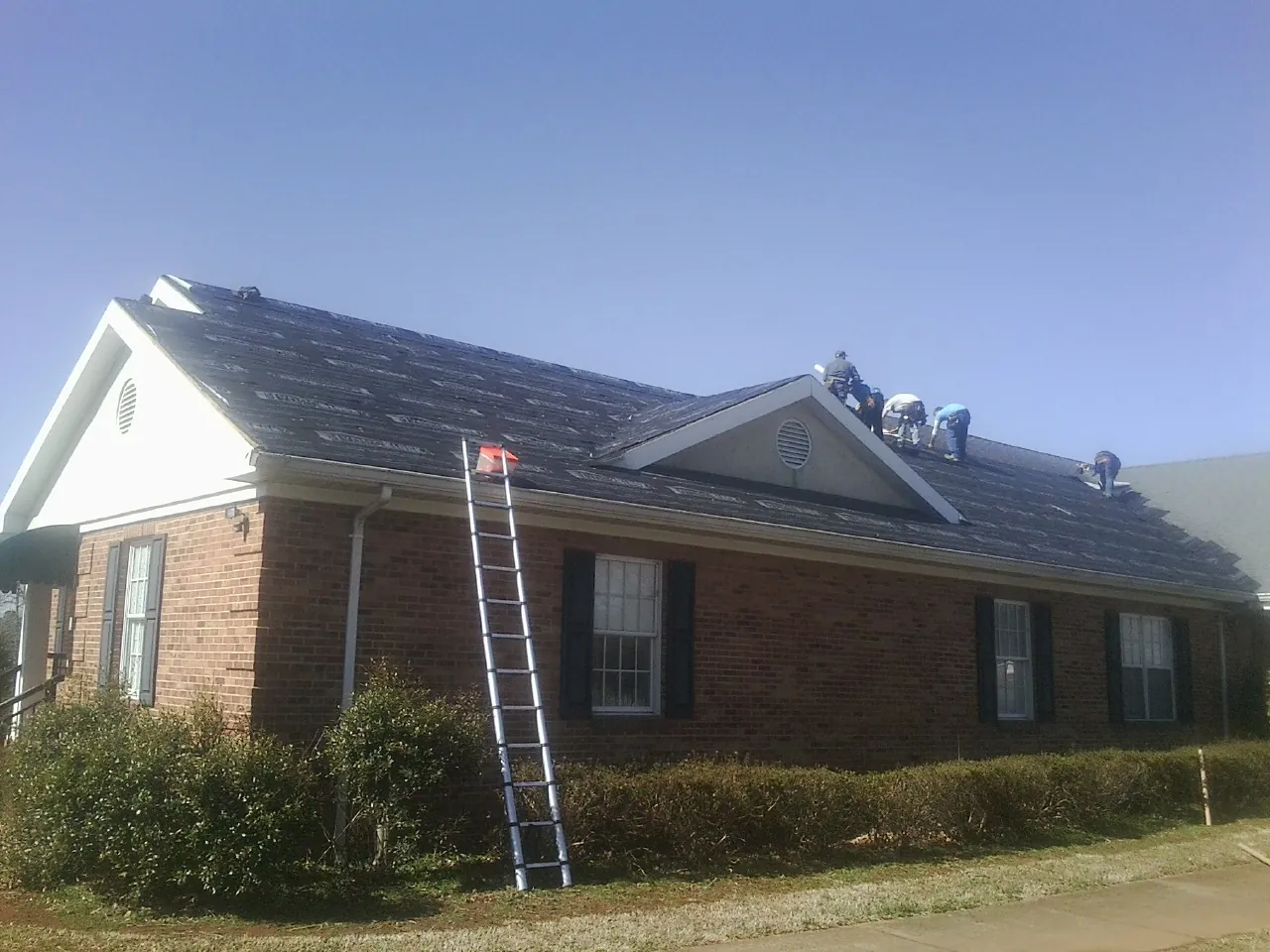 Crew tearing shingles off a brick ranch roof with a ladder set — Emergency Roof Repair work by our crew in Lucedale