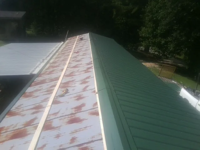 Old rusted panels beside newly installed green metal roofing — Wind Damage Roof Repair by Roofing Brothers in Lucedale