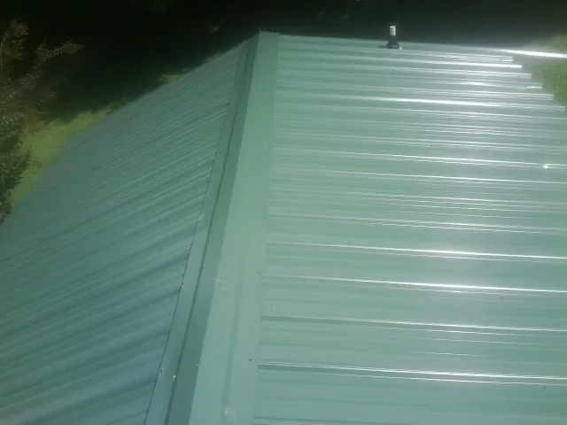 New green metal panels meeting at the ridge of a roof — Flat Roof Repair work by our crew in Lucedale