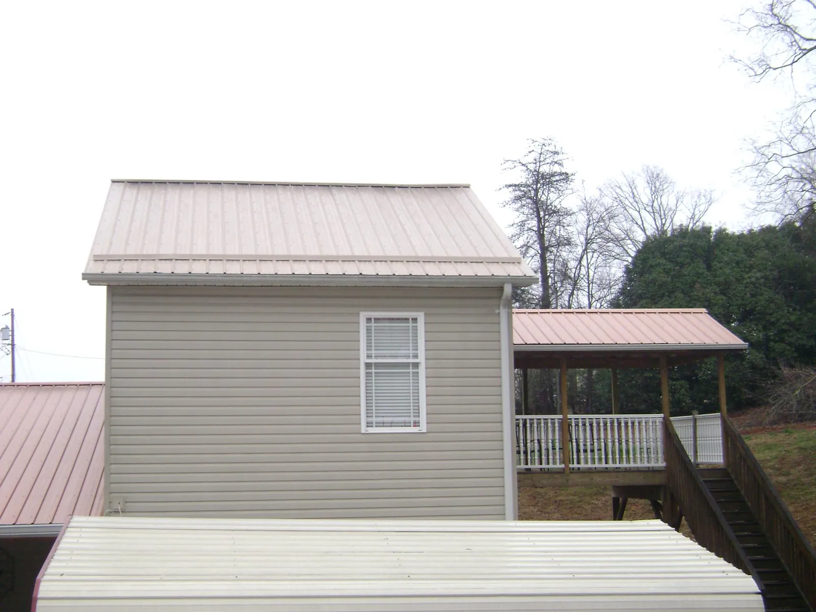 Tan metal roofs on a two story addition and attached porch, from a Roof Replacement job in Lucedale